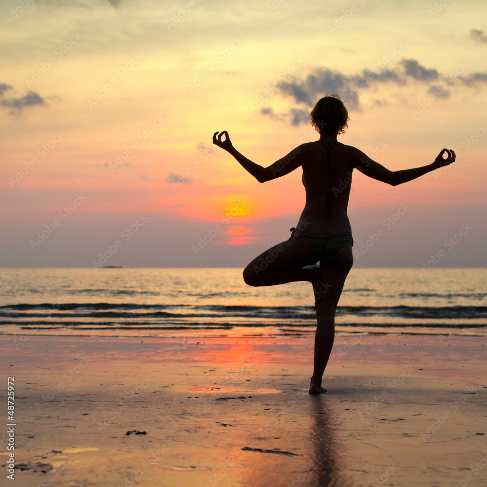 Yoga woman performs an exercise on the beach during sunset.