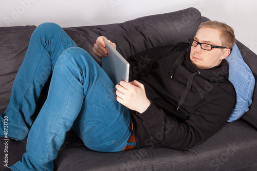 Ein junger Mann liegt auf einem Sofa und hat ein Tablet-PC in de
