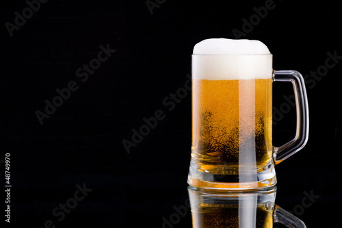 фотографія Mug fresh beer with cap of foam on a black background