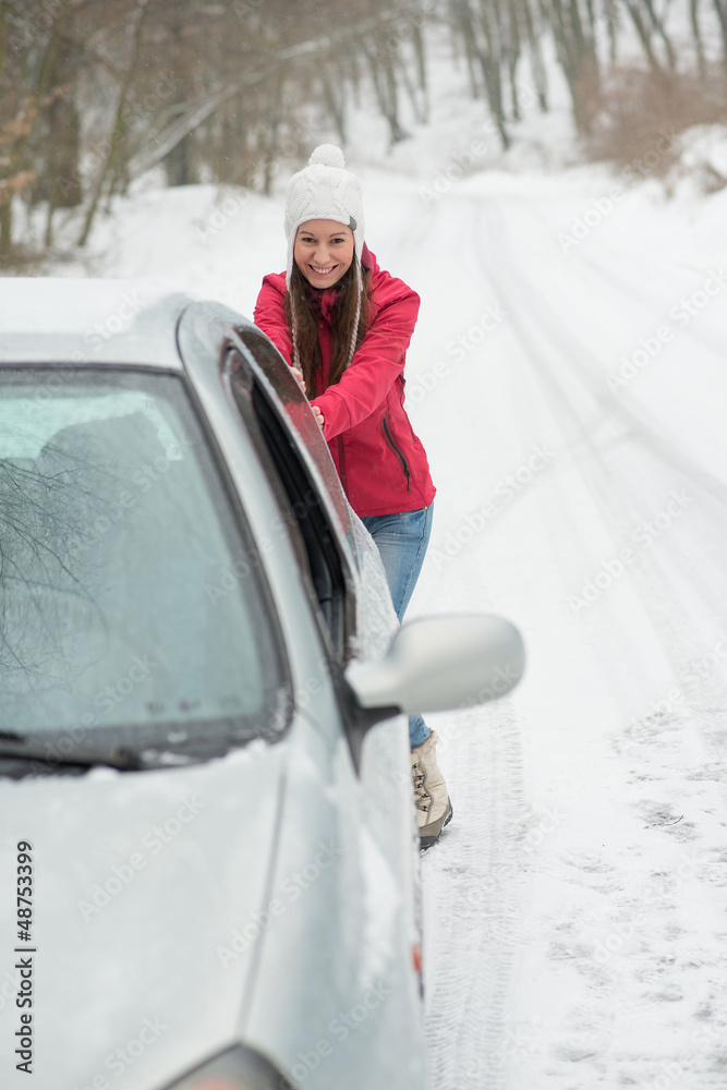 The girl is pushing a broken car on the road in winter