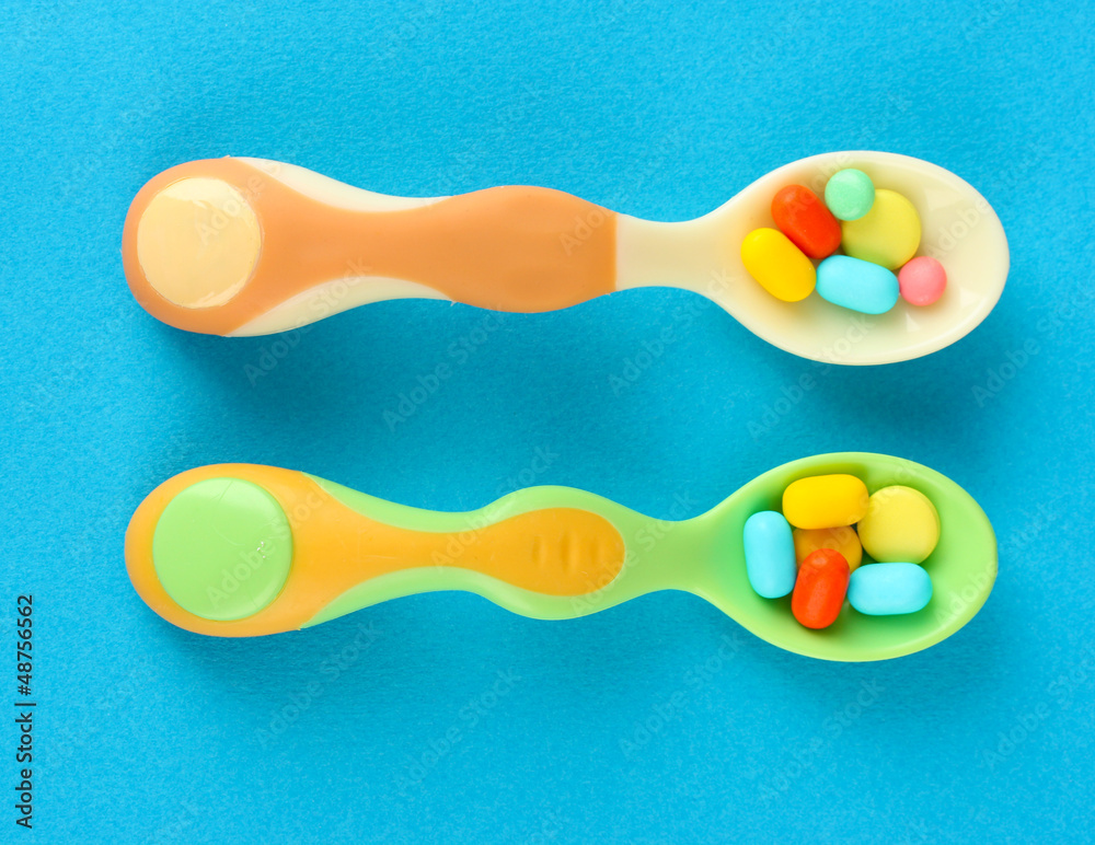 Plastic spoons with color pills on blue background Plastic spoons with color pills on blue background