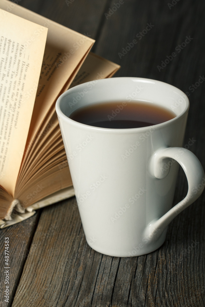 Cup of tea with old opened book on wooden table. Cup of tea with old opened book on wooden table.