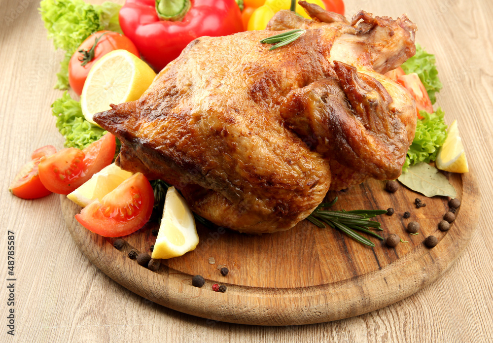 Whole roasted chicken with vegetables on plate, on wooden table Whole roasted chicken with vegetables on plate, on wooden table