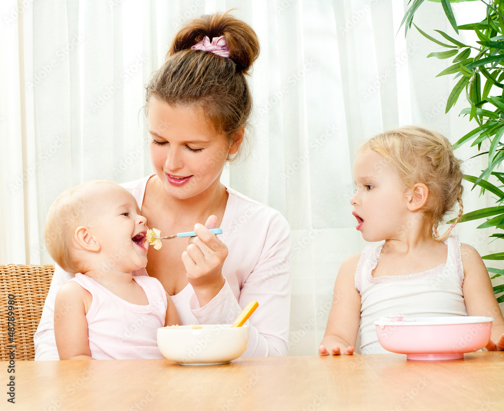 young mother feeding her two daughters from a spoon young mother feeding her two daughters from a spoon