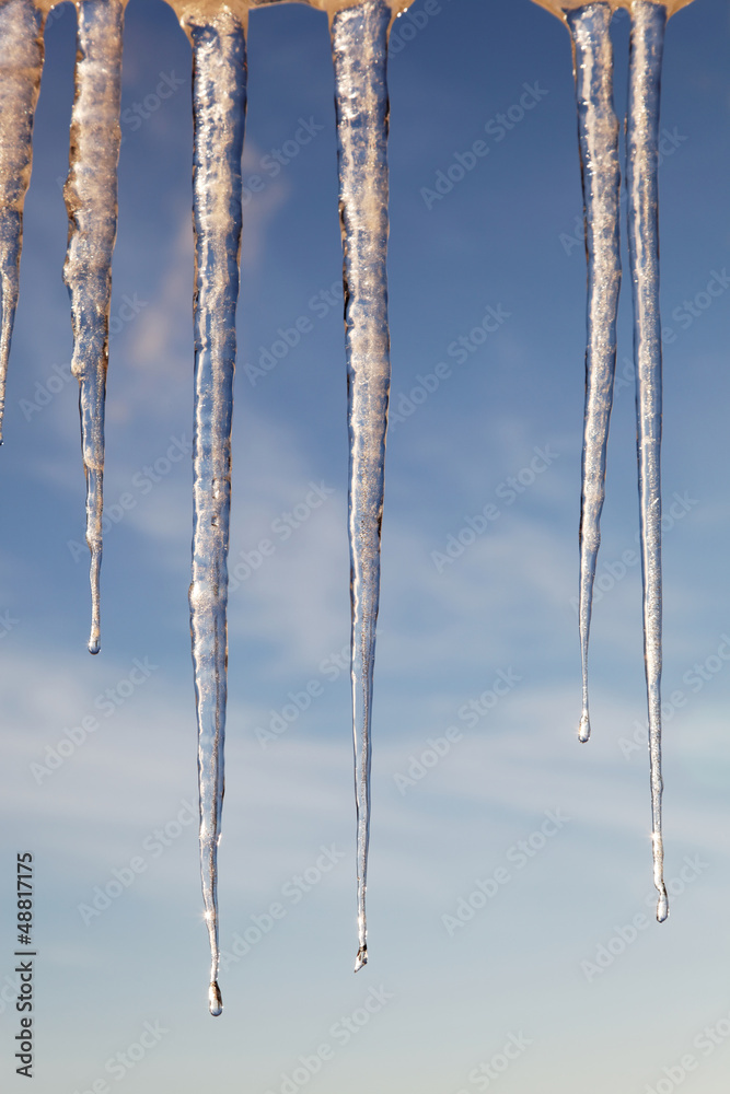 Icicles in the sunny day against a blue sky with white clouds. Icicles in the sunny day against a blue sky with white clouds.