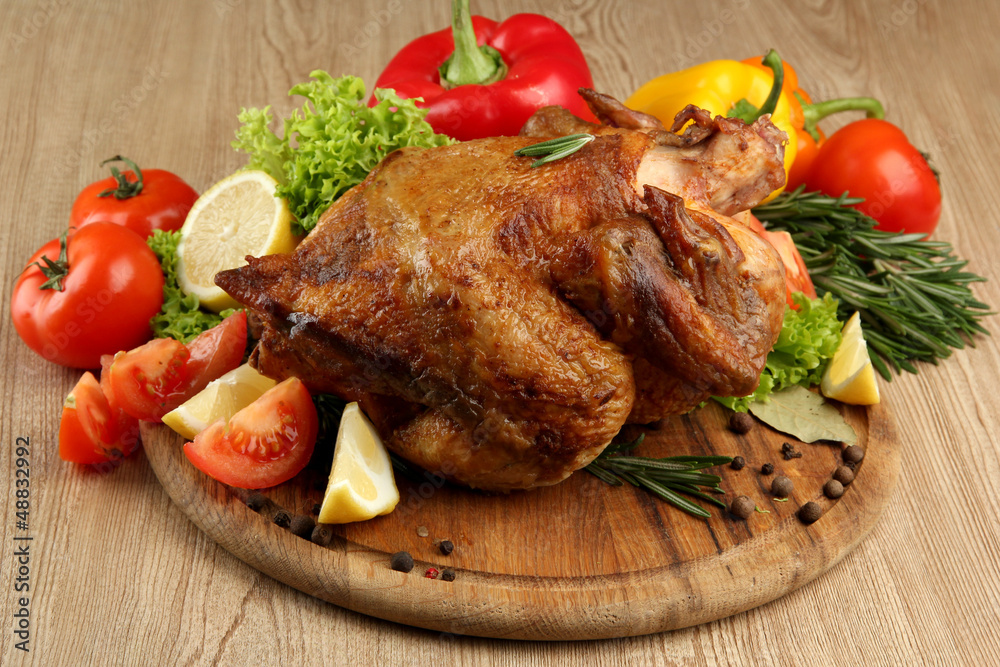 Whole roasted chicken with vegetables on plate, on wooden table Whole roasted chicken with vegetables on plate, on wooden table