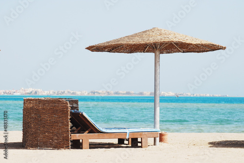 empty beach chair with straw sunshade at the sea