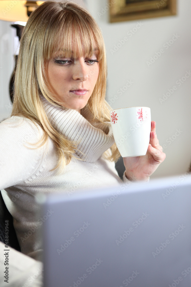 cute young blonde having coffee while working on laptop cute young blonde having coffee while working on laptop