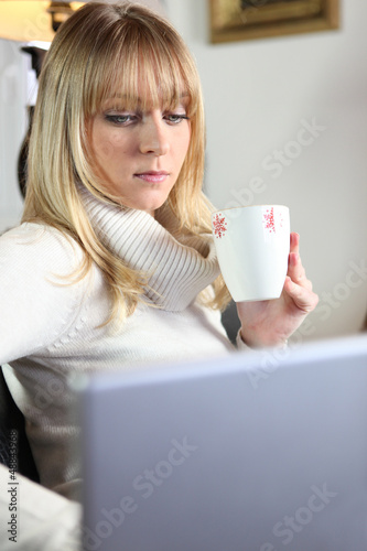 cute young blonde having coffee while working on laptop