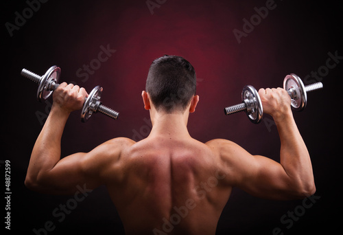 Muscular young man lifting weights against black background