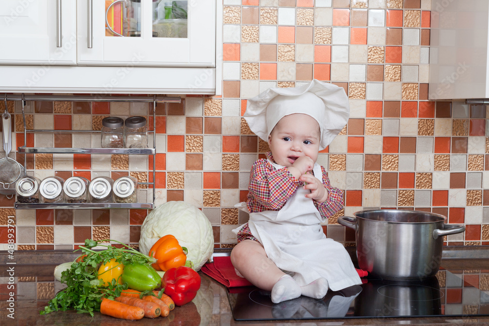 baby cook with vegetables sits on a kitchen table