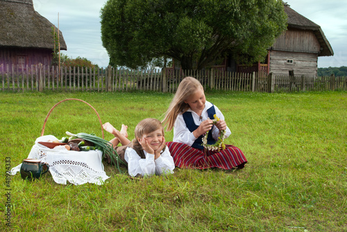 Little boy and girl sitting on a lawn in a national latvian clot