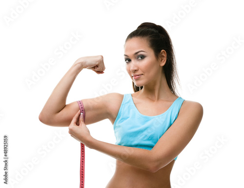 Fototapeta Sporty woman measures her bicep with measuring tape