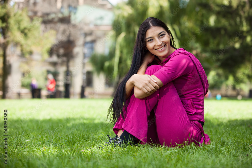 Happy young girl sitting on grass in park Happy young girl sitting on grass in park
