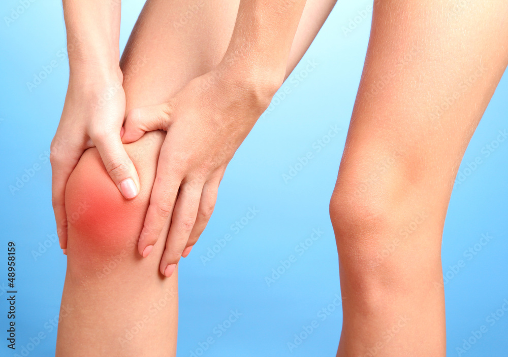woman holding sore knee, on blue background