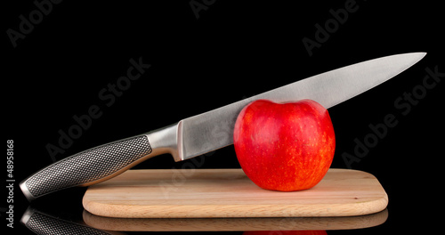 Red apple and knife on cutting board, isolated on black photo