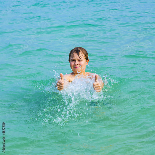 handsome boy has fun in the ocean and shows thumbs up