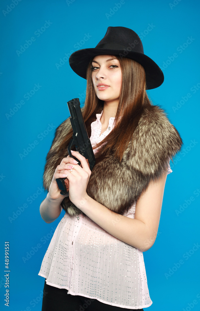 A serious young  girl in a black hat with a gun in his hand