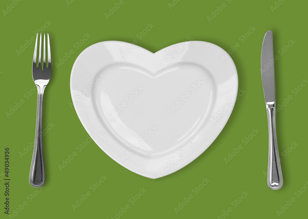 plate in shape of heart, table knife and fork on green backgroun plate in shape of heart, table knife and fork on green backgroun