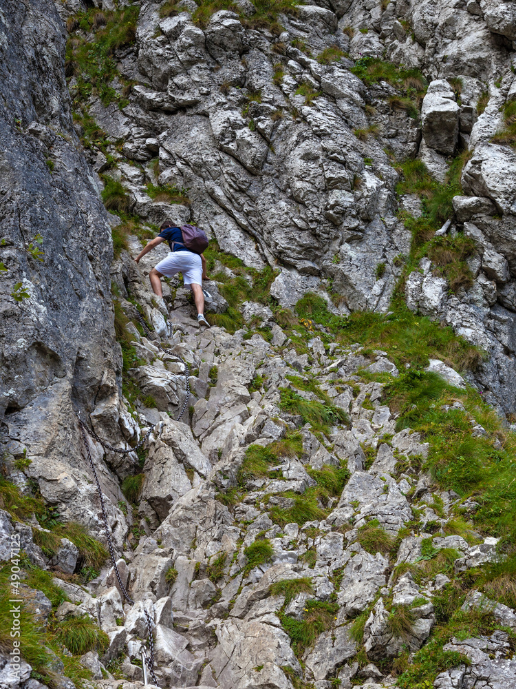 Man climbing a rock difficult and dangerous path using chains.