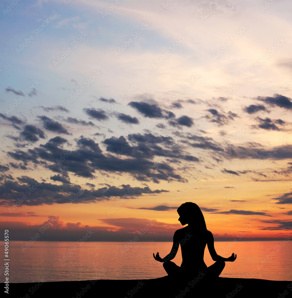 A silhouette of a young woman meditation on the beach