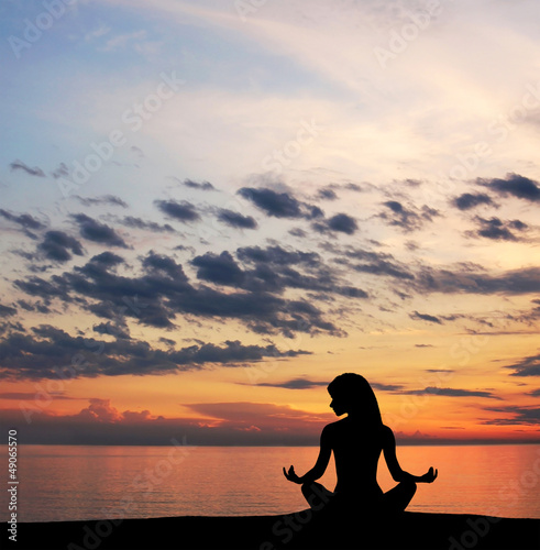 A silhouette of a young woman meditation on the beach © Acronym