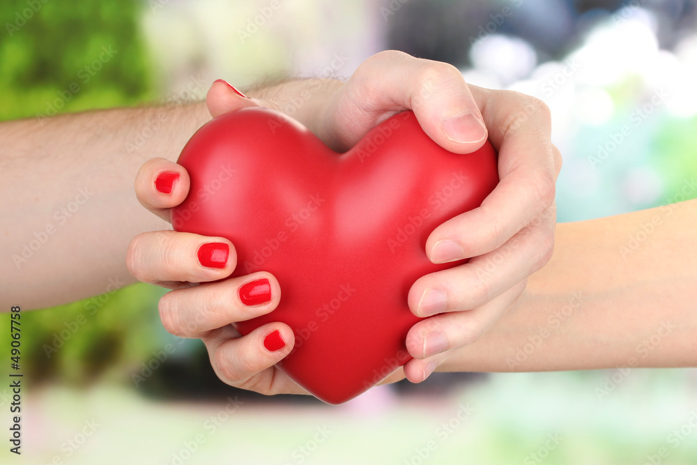 Red heart in woman and man hands, on green background Red heart in woman and man hands, on green background