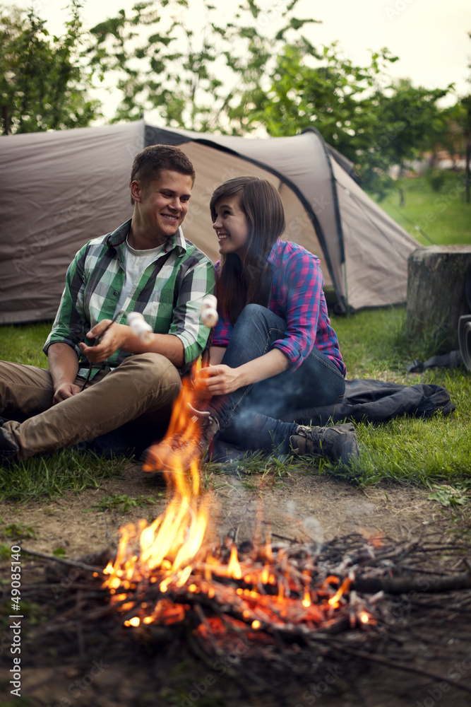Young couple sitting near a campfire and toasting marshmallow Young couple sitting near a campfire and toasting marshmallow