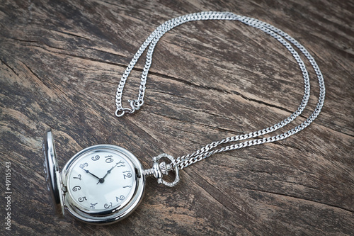 Silver pocket watch on chain, a wooden texture.