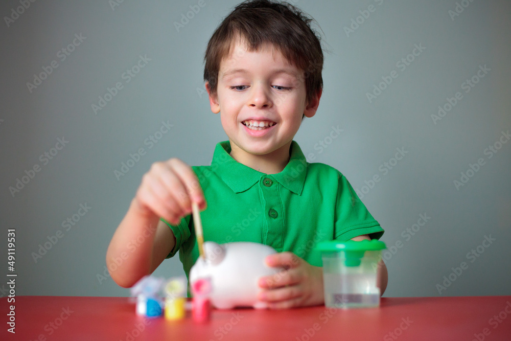 Cute happy little boy painting his piggy toy Cute happy little boy painting his piggy toy