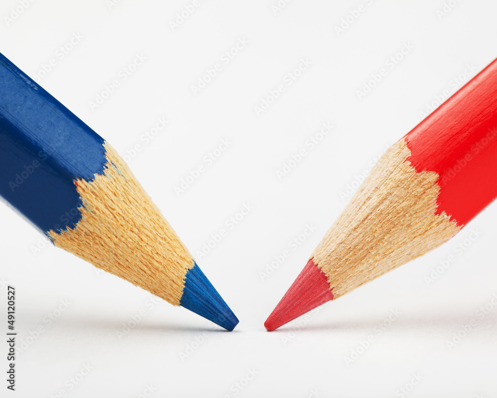 Obraz premium red and blue pencils against each other on a white paper sheet