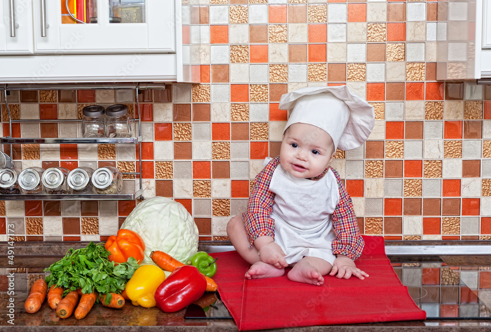 Baby cook with vegetables sits on a kitchen table Baby cook with vegetables sits on a kitchen table