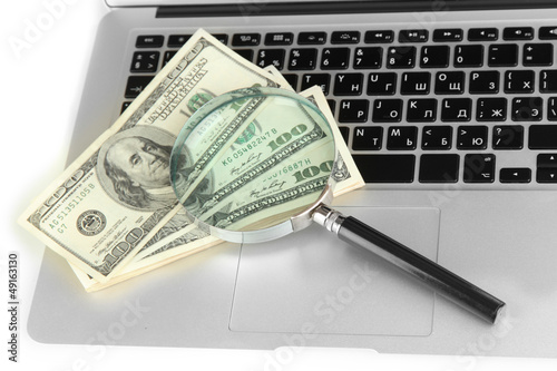 Money with magnifying glass on laptop close-up