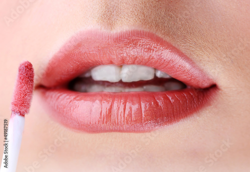 Beautiful young woman applying lip gloss, close up.