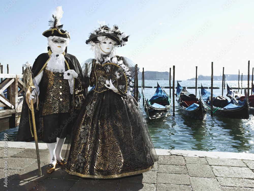 Two masks at the Venice carnival in front of gondolas