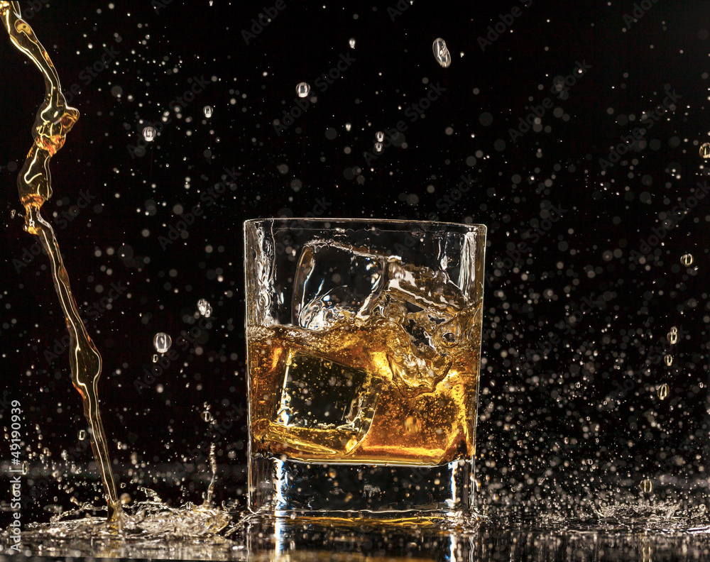 Whiskey splashing around glass, isolated on black background