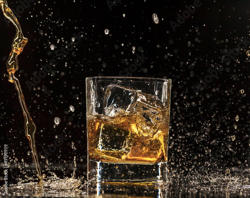 Whiskey splashing around glass, isolated on black background