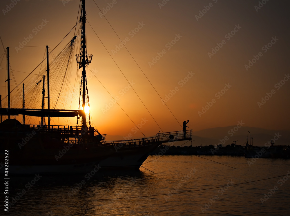 Sailing ship silhouetted against amber setting sun