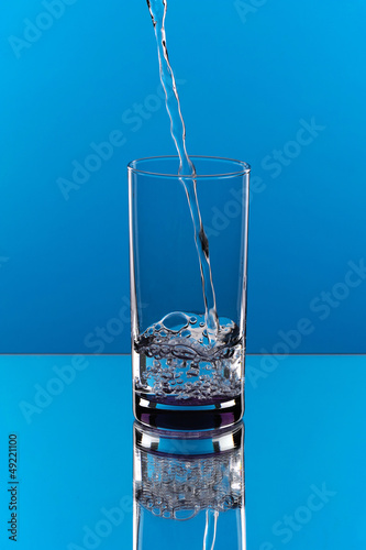 Pouring water in a glass isolated blue background