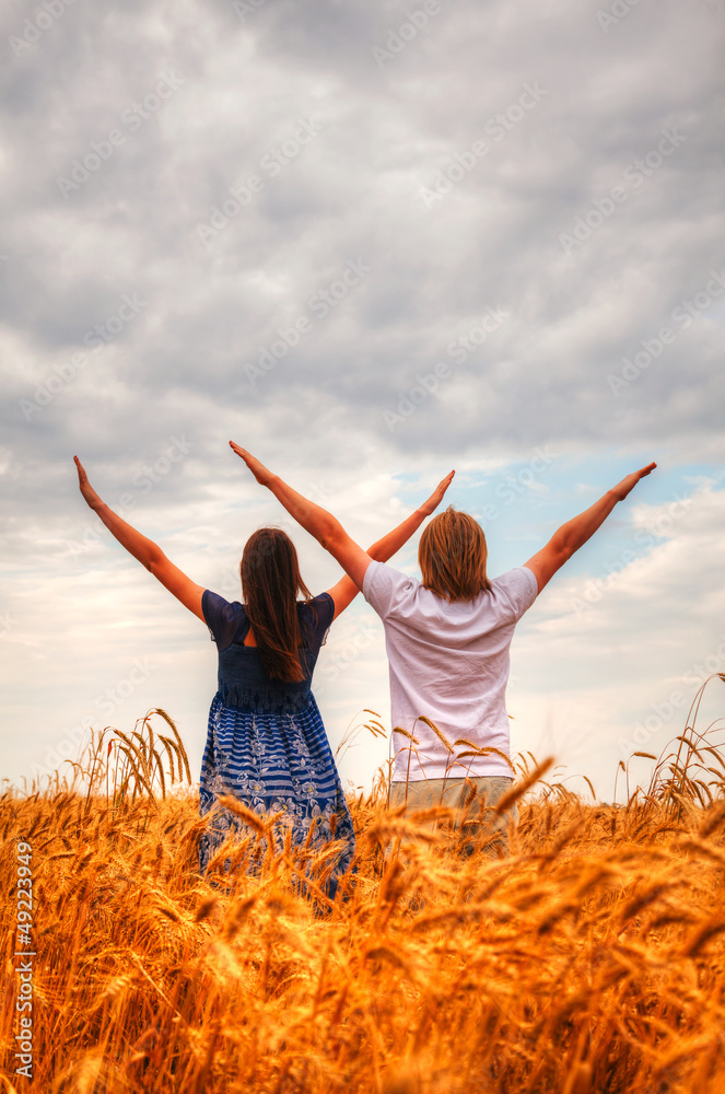 Couple staying with raised hands at a wheat field