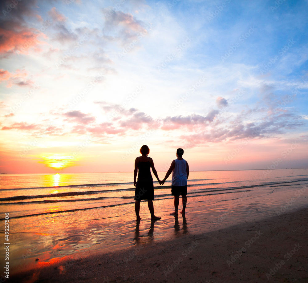 Young couple holding hands on the sea beach at sunset.