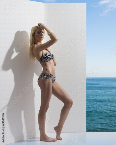 blonde girl in bikini near the wall with hand on the head