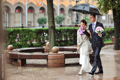 Bride and groom couple walking together in a rainy day