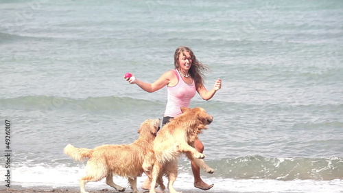 Beautiful happy woman playing with two dogs at beach
