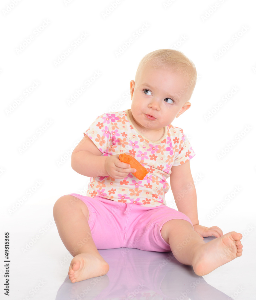 Sweet little baby eating a carrot sitting on the floor on white Sweet little baby eating a carrot sitting on the floor on white