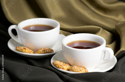 Two white cups of tea and cookies with sesame seeds