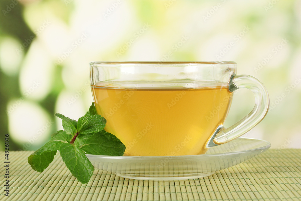 Cup of tea with mint on table on bright bacground