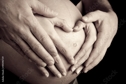 hands of pregnant woman and her husband in heart shape on her be #49390739