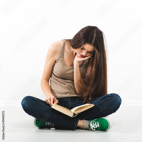 Beautiful young woman sitting on floor with book