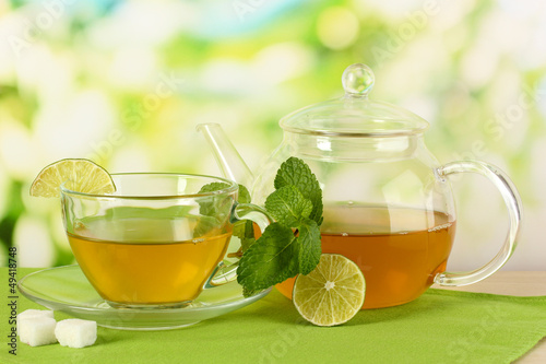 Cup of tea with mint and lime on table on bright background